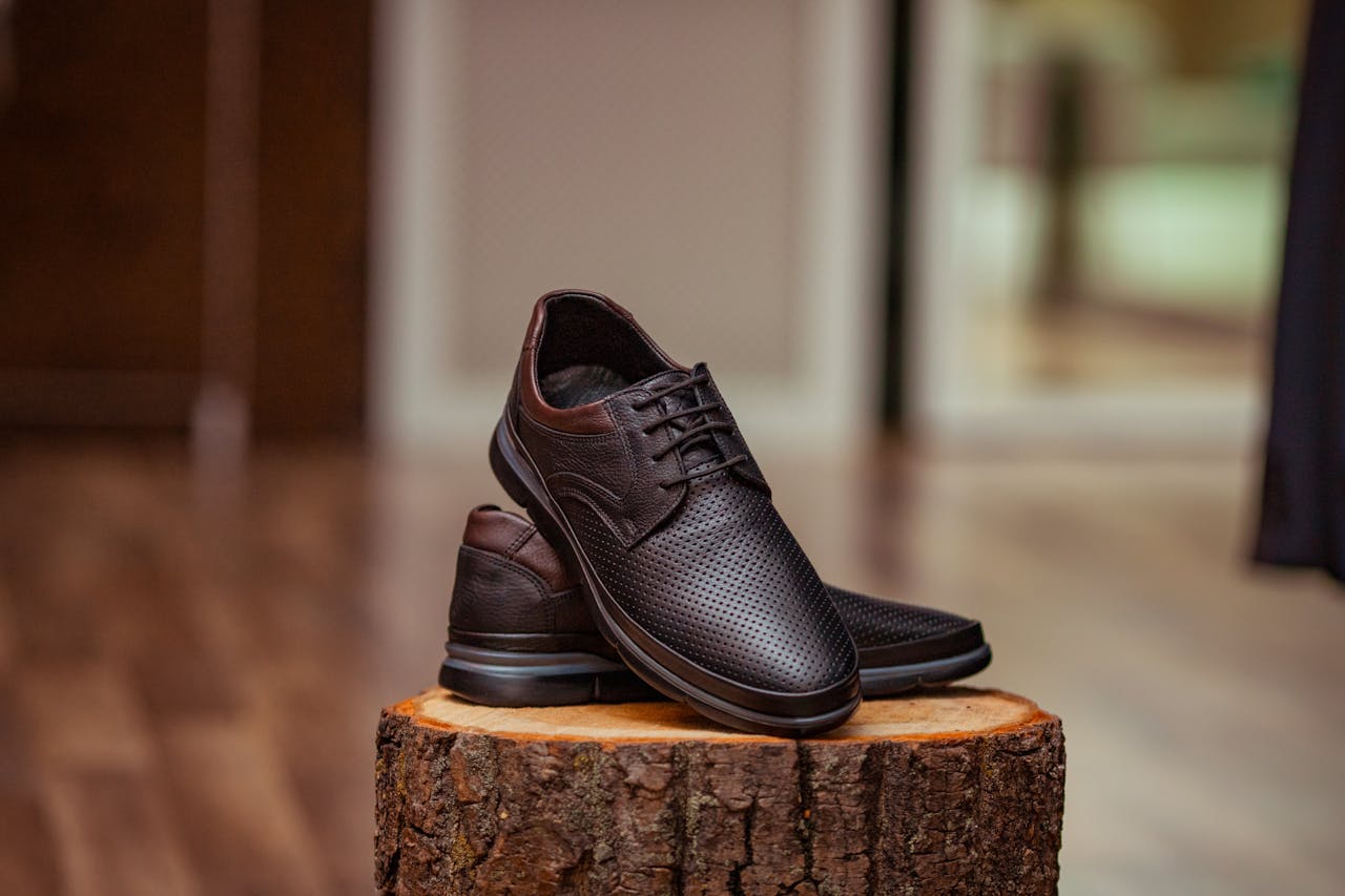 gallery-02 Stylish perforated leather shoes displayed elegantly on a rustic wooden stump indoors.